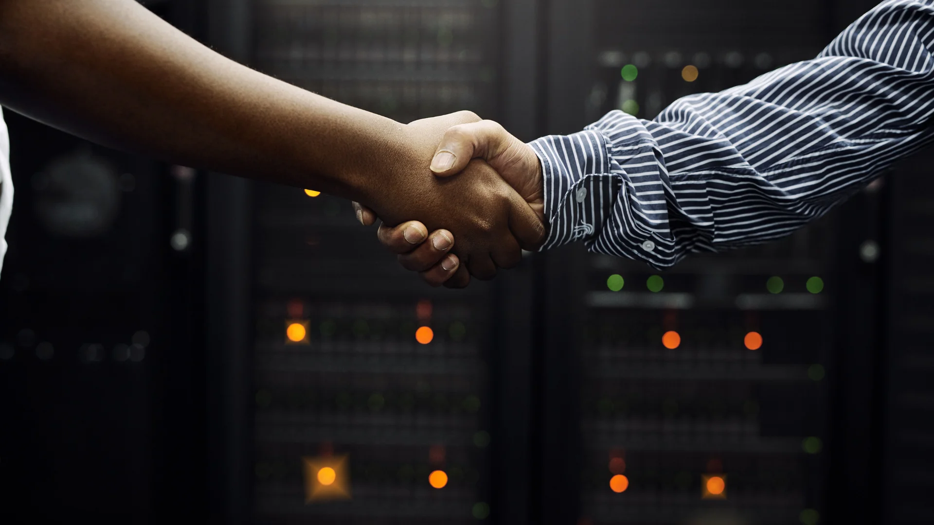 Two people shaking hands in front of server rack