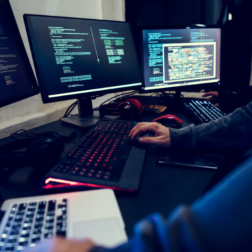 User holding mouse working at desk with three screens