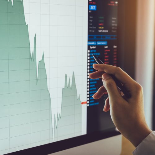 Close up of businessman hand pointing to stock market chart and analysis on computer screen.