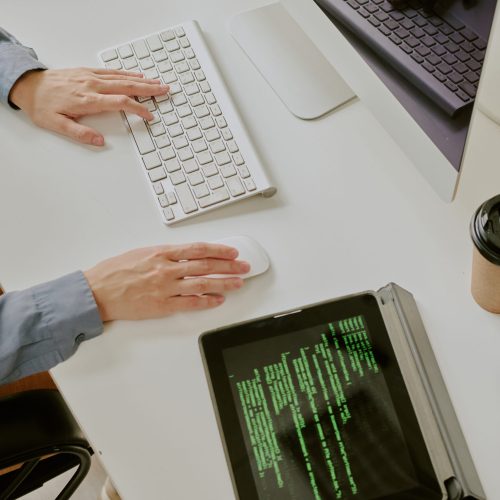 High angle view of hands of unrecognizable female programmers hands typing code on desktop computer keyboard and using wireless mouse in office